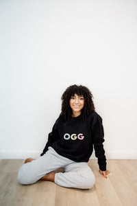 woman wearing black crewneck with the OGG airport code written on the front in colourful graphics
