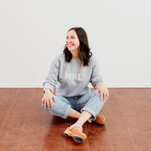 Load image into Gallery viewer, Woman is wearing a grey crewneck with colourful letters HNL on the front 
