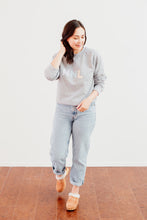 Load image into Gallery viewer, Woman is wearing a grey crewneck with colourful letters HNL on the front
