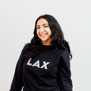 Woman is wearing a black crewneck with LAX written on the front in colourful letters