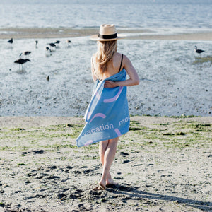 Woman is holding a blue and pink beach towel with words 'vacation mode' witten on it