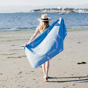 Woman is holding a blue and pink beach towel with words 'vacation mode' witten on it